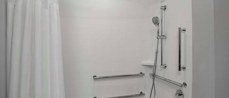 A modern bathroom with white tiled walls, a bathtub, a shower with multiple fixtures, and grab bars.