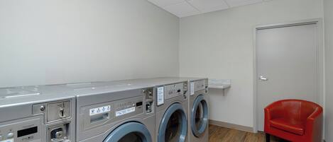 A laundry room with three front-loading washing machines, a red chair, and a door.