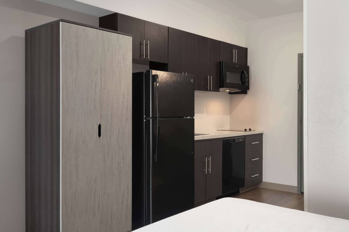 A modern kitchen with dark cabinets, a black refrigerator, and a microwave.