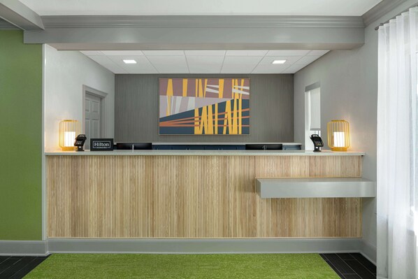 A reception desk with a modern design, featuring a wooden panel backdrop and a large abstract artwork above it. - Spark by Hilton Destin (Destin)