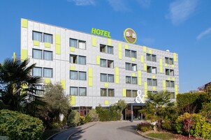 Un moderno edificio de hotel con un letrero que dice "HOTEL" y el logotipo "B&B". Presenta una fachada simétrica con varias ventanas y una entrada central.