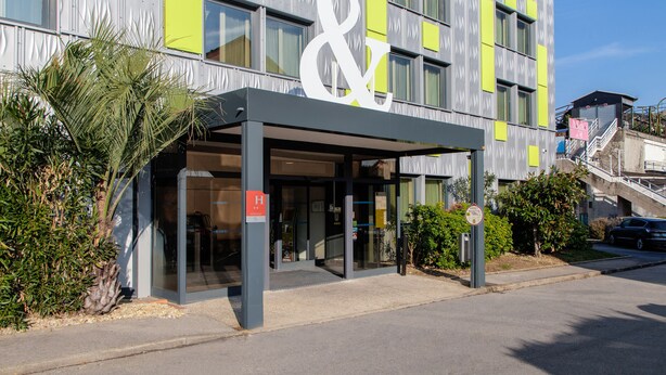 A modern building with a prominent '&' sign above the entrance, indicating a commercial establishment. - B&B HOTEL Orly Rungis Aéroport (Rungis)