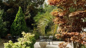 An outdoor patio area with a stone table and chairs, surrounded by various trees and shrubs. - B&B HOTEL Orly Rungis Aéroport (Rungis)