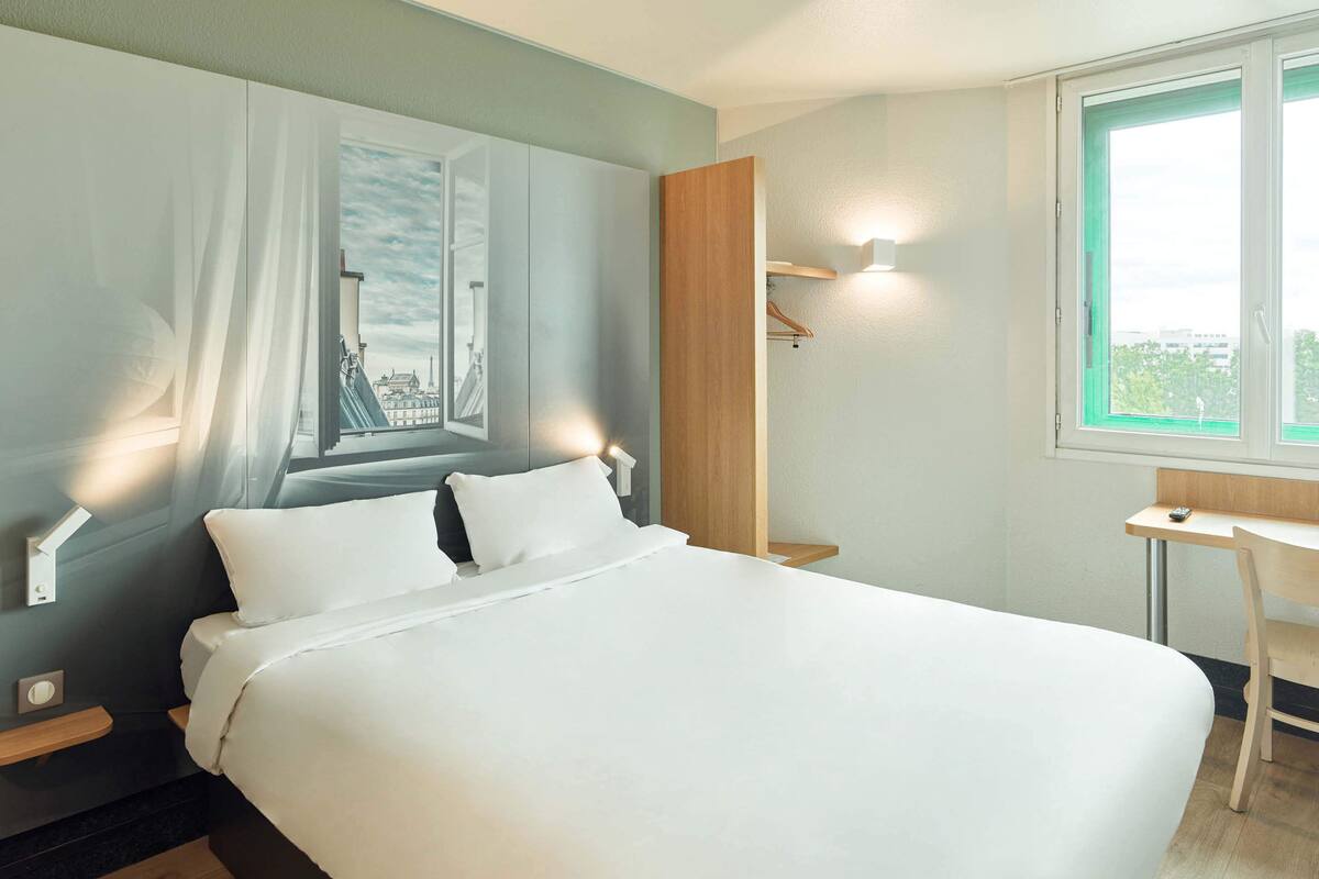 Una habitación de hotel con cama, escritorio, silla, armario y ventana con vistas.