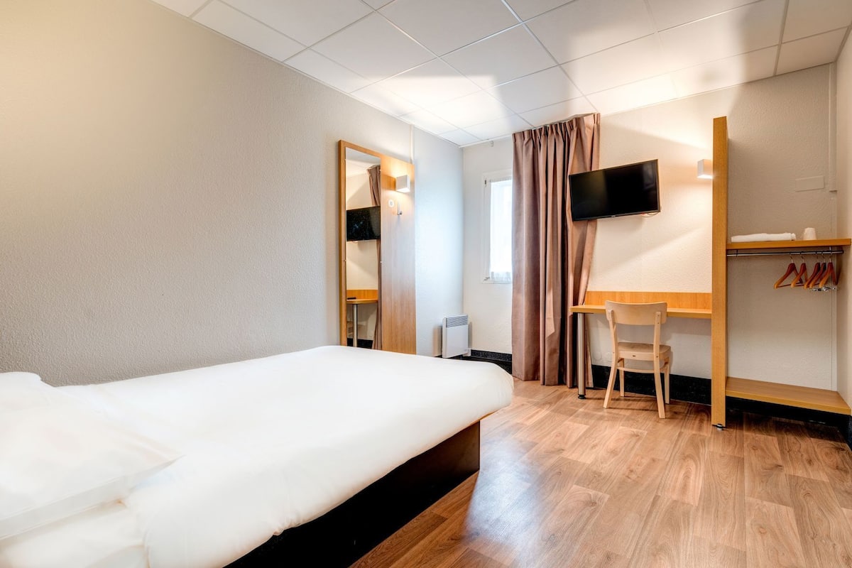 Habitación de hotel con cama, escritorio, silla, televisión y armario.