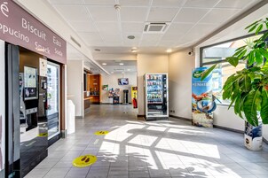 A clean, well-lit indoor area with a vending machine, a snack shop, and a large potted plant.