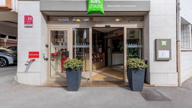 Entrada de un hotel con un cartel que dice 'ibis Styles Hotels Marseille Casteleane', un hidrante y dos macetas.
