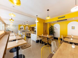 A modern restaurant interior with multiple dining tables and chairs, a kitchen area, and yellow walls. - ibis Styles Marseille Centre Prado Place Castellane (Marseille)