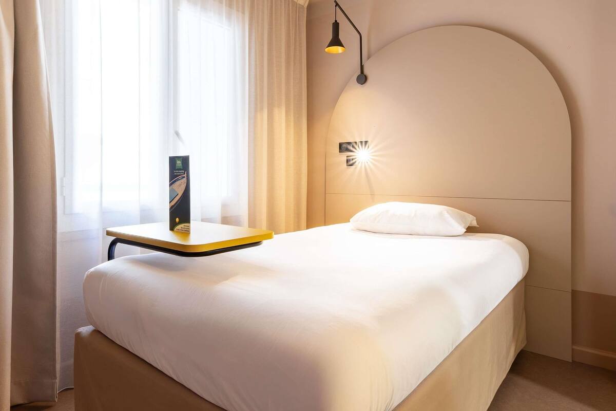 Une chambre d’hôtel avec un lit, une table de chevet, une lampe et une fenêtre avec des rideaux.