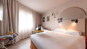 Una habitación de hotel con cama, escritorio, silla, maleta y ventana con cortinas.