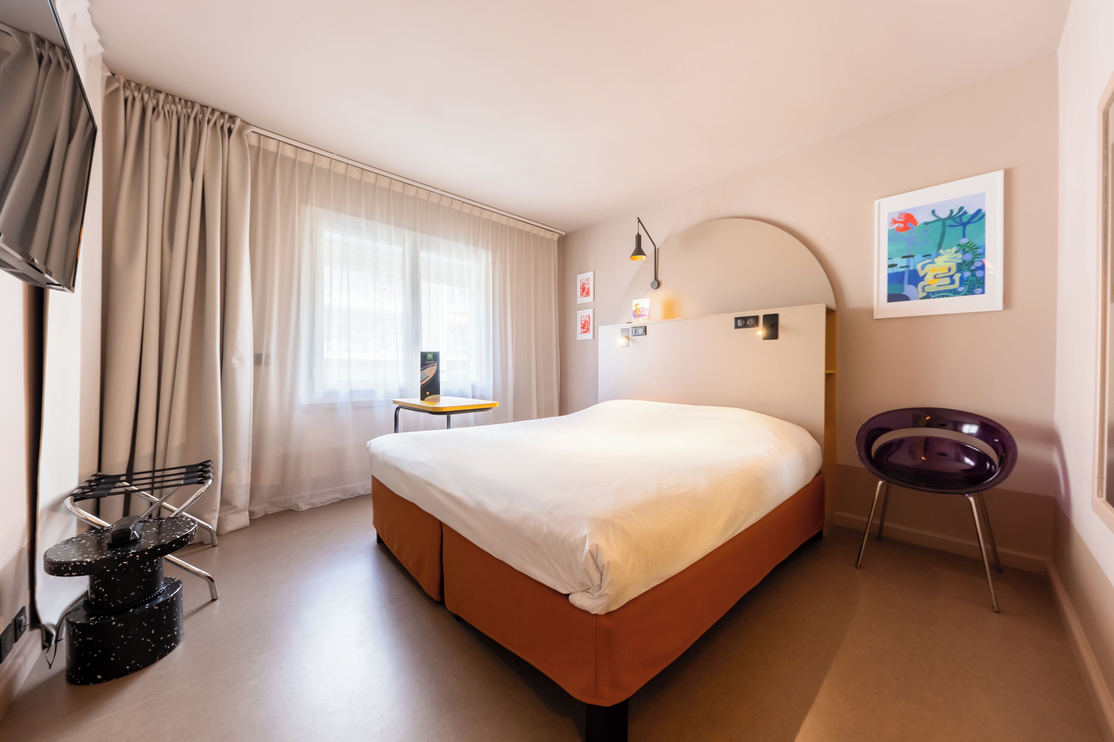 A hotel room with a bed, a desk, a chair, and a TV.