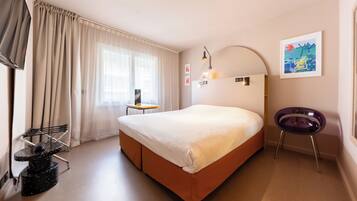 A hotel room with a bed, a desk, a chair, and a TV.