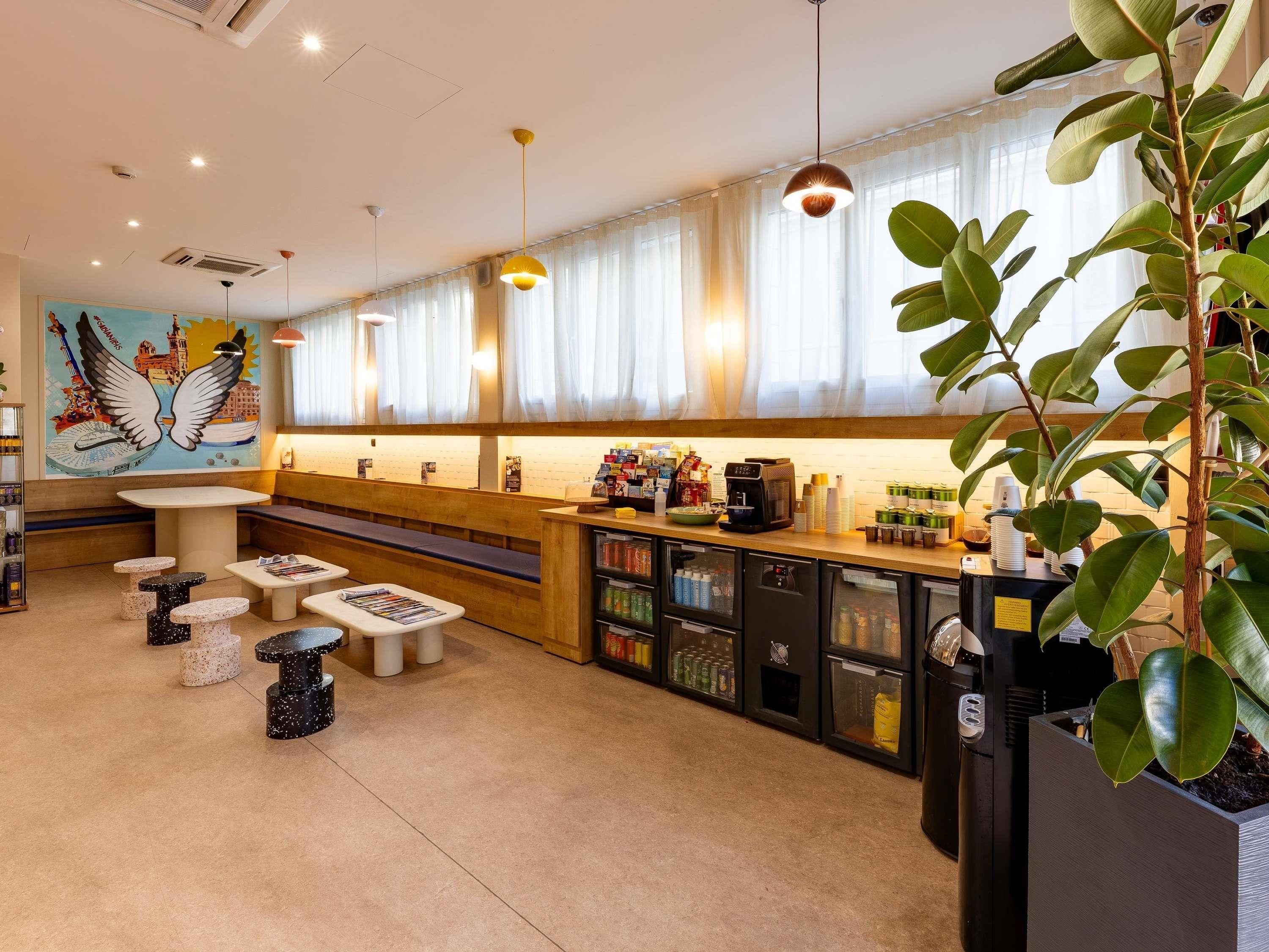 Café com mesas e cadeiras, balcão com bebidas e um mural na parede.