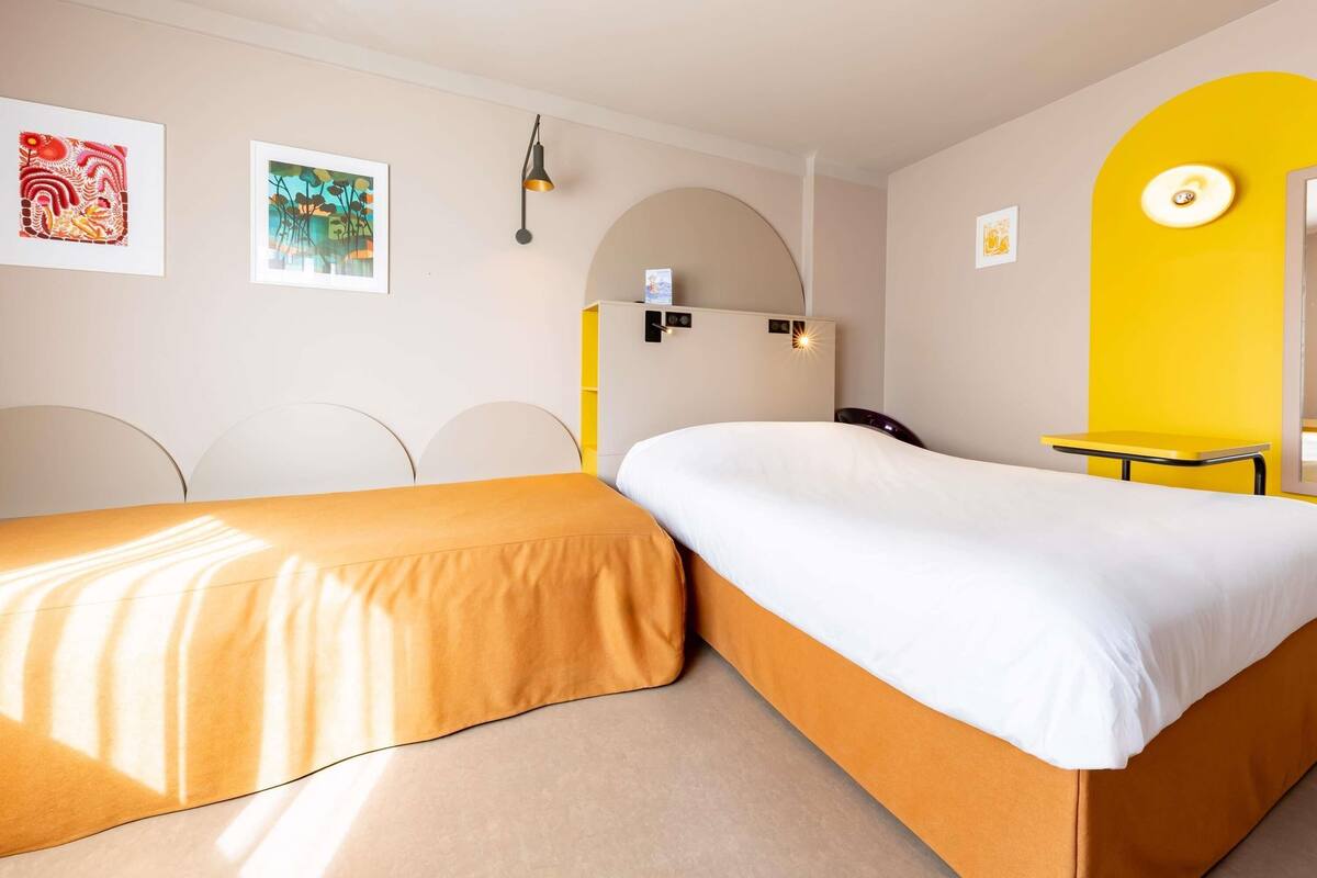 Une chambre d’hôtel avec deux lits, un bureau et des œuvres d’art accrochées aux murs.