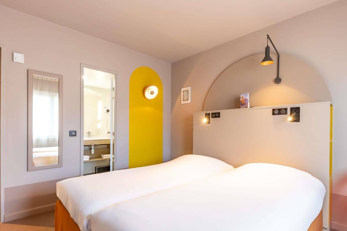 Une chambre à coucher avec un lit, un miroir, une porte et un luminaire fixé au mur.