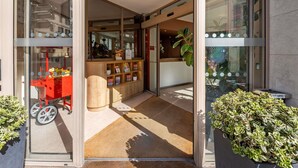 Entrada de hotel con mostrador de recepción, un carrito rojo y plantas en macetas.