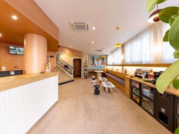 Een hotel lobby met een receptiebalie, een trap, een zithoek en een toonbank met diverse artikelen.
