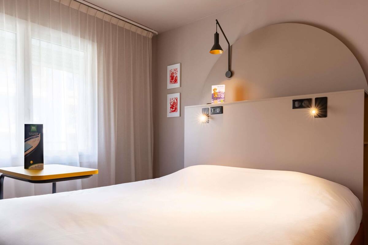 Une chambre d’hôtel avec un grand lit, une petite table, un bureau et un luminaire fixé au mur.