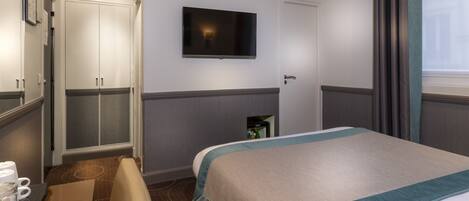 A hotel room with a bed, a television mounted on the wall, a wardrobe, and a small cabinet.