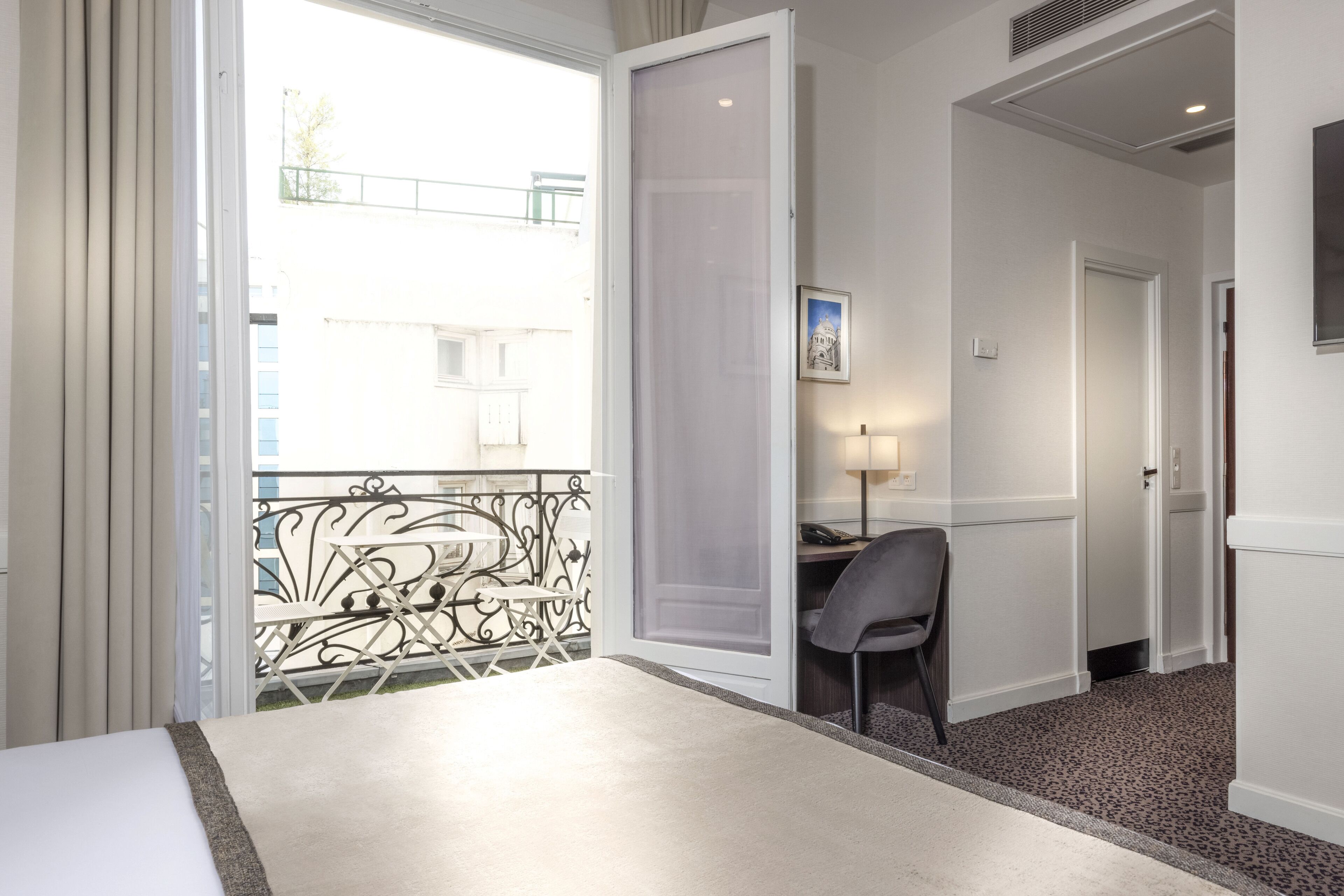 Una camera d'albergo con un letto, una scrivania, una sedia e un balcone con ringhiera.