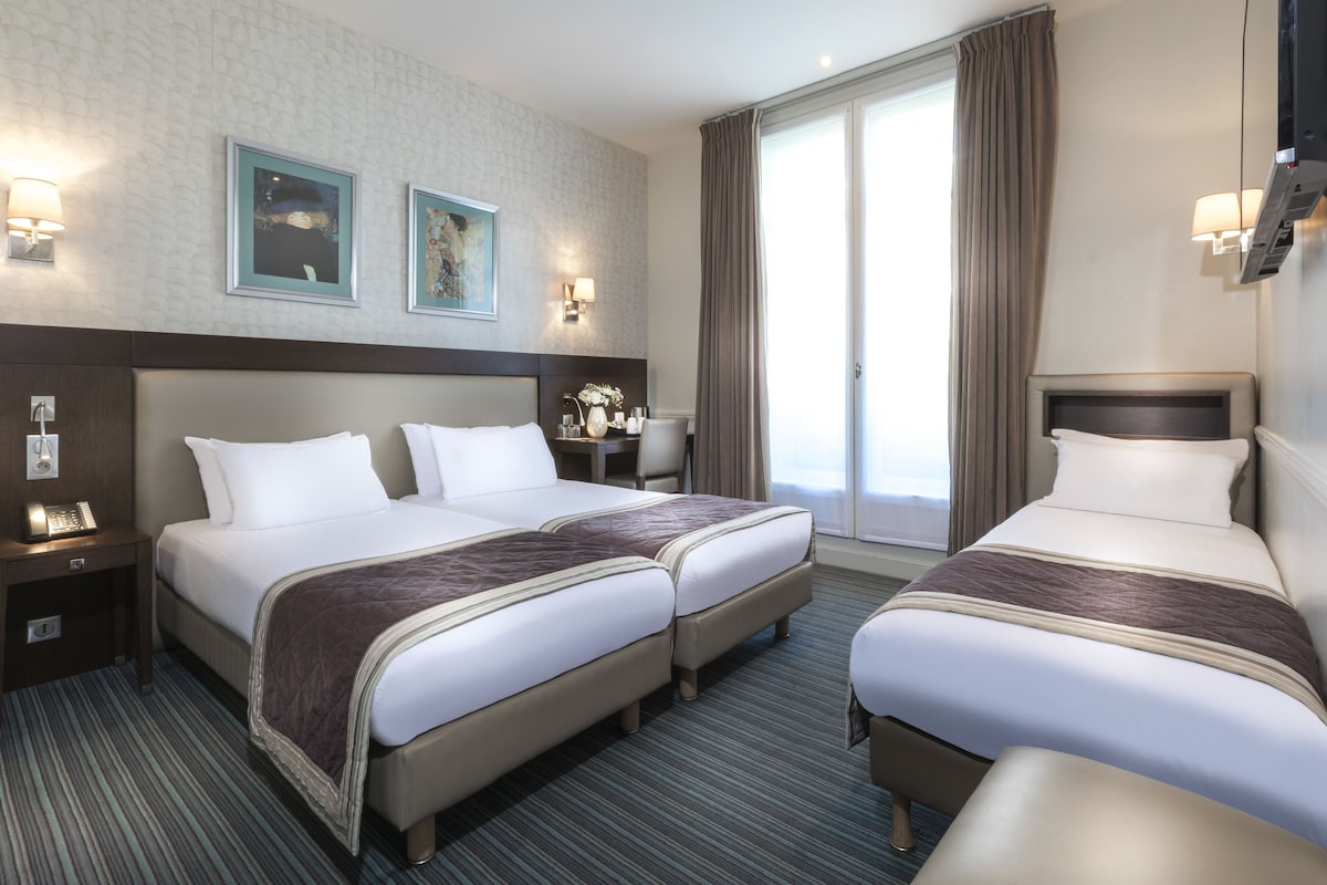 A hotel room with two beds, a desk, a chair, a lamp, and a TV.