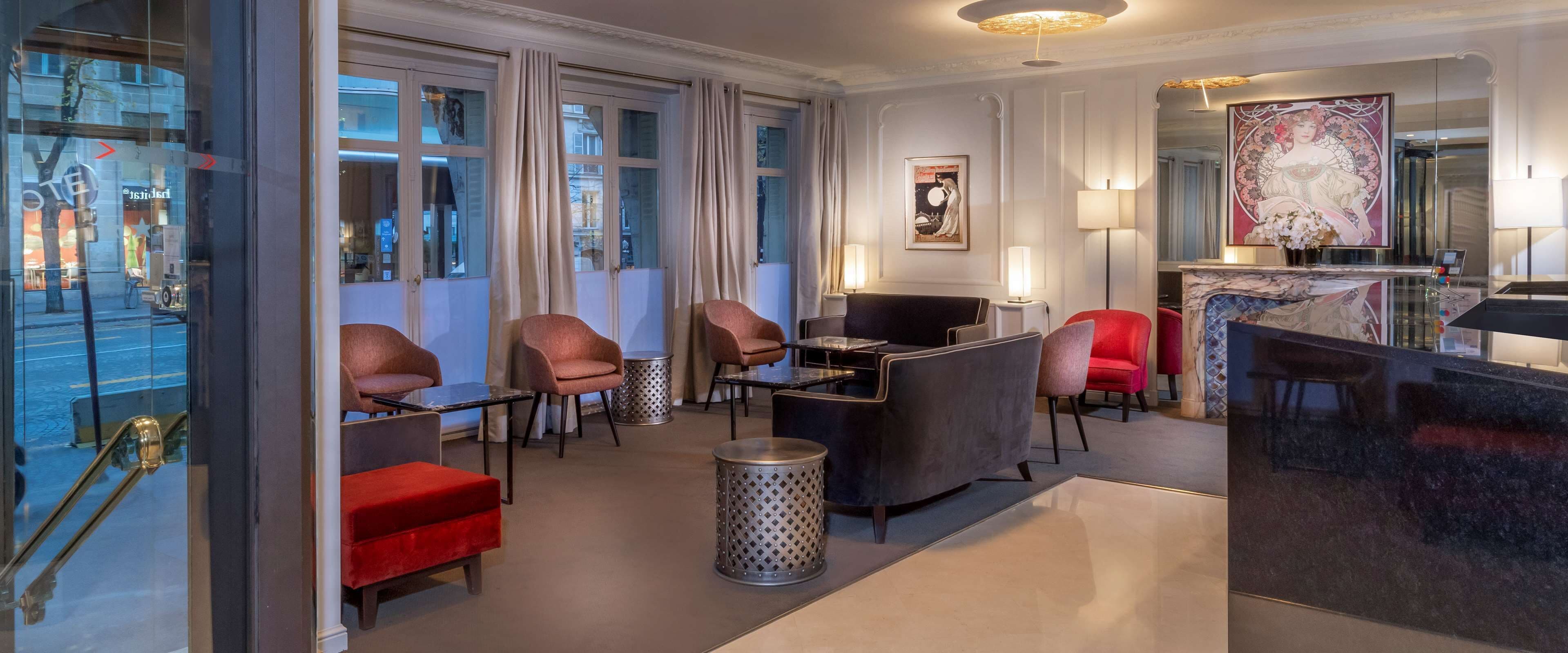A modern hotel lobby with a seating area, a reception desk, and a large window with curtains.
