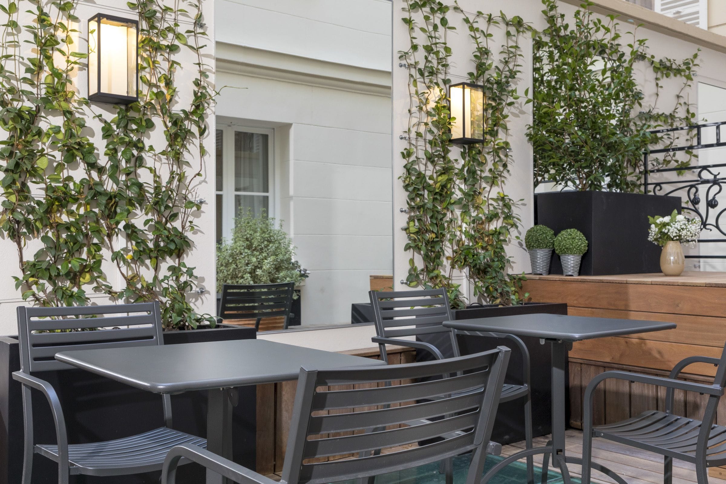 Un espace extérieur aménagé avec des tables et des chaises, entouré de verdure et illuminé par un éclairage décoratif.