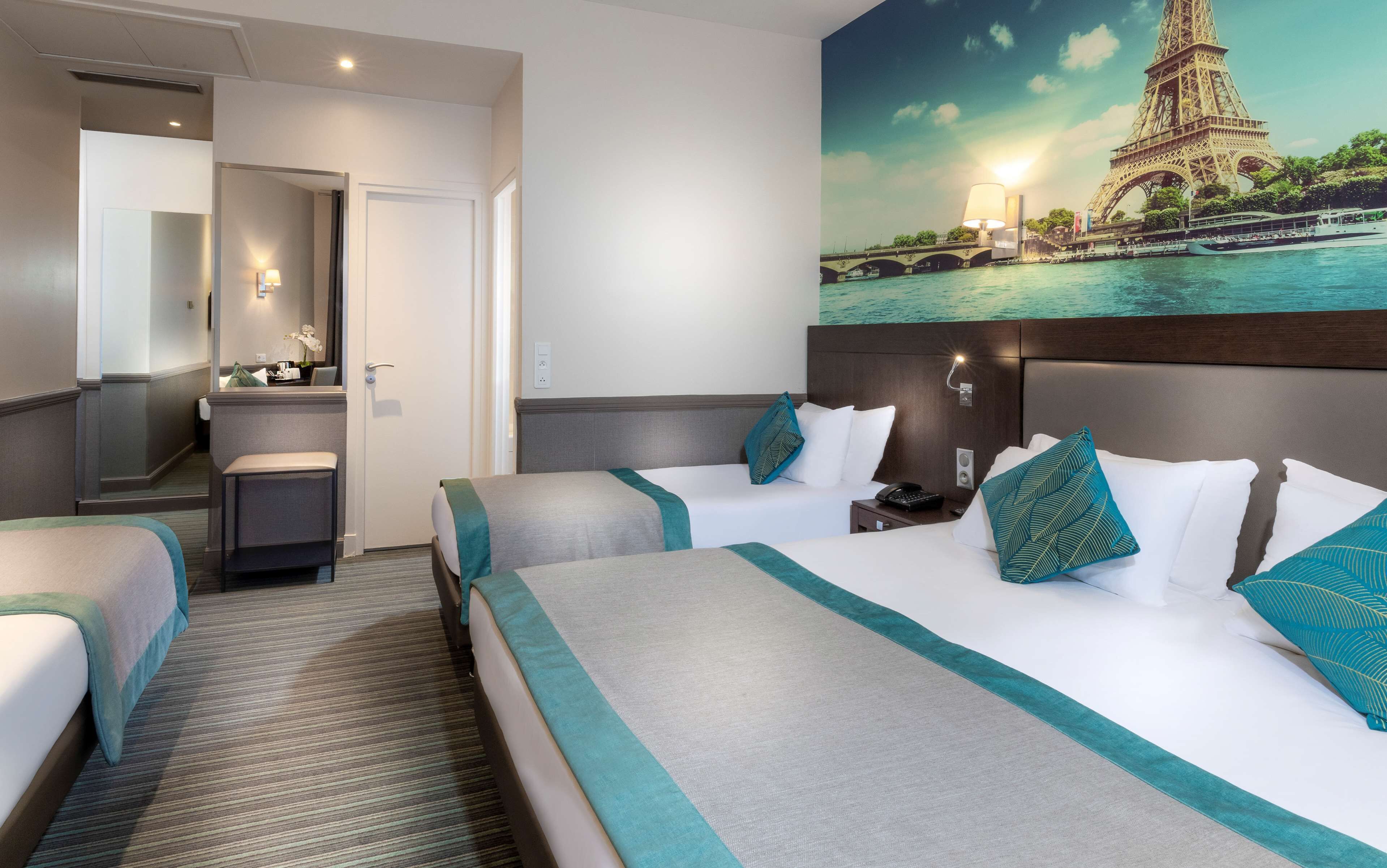 Une chambre d’hôtel avec deux lits, une salle de bain et un grand tableau représentant la Tour Eiffel.