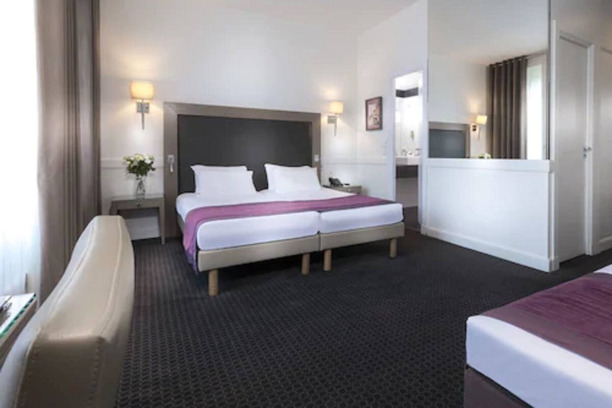 Une chambre d’hôtel avec un lit double, deux tables de chevet, une commode, un bureau et une chaise.