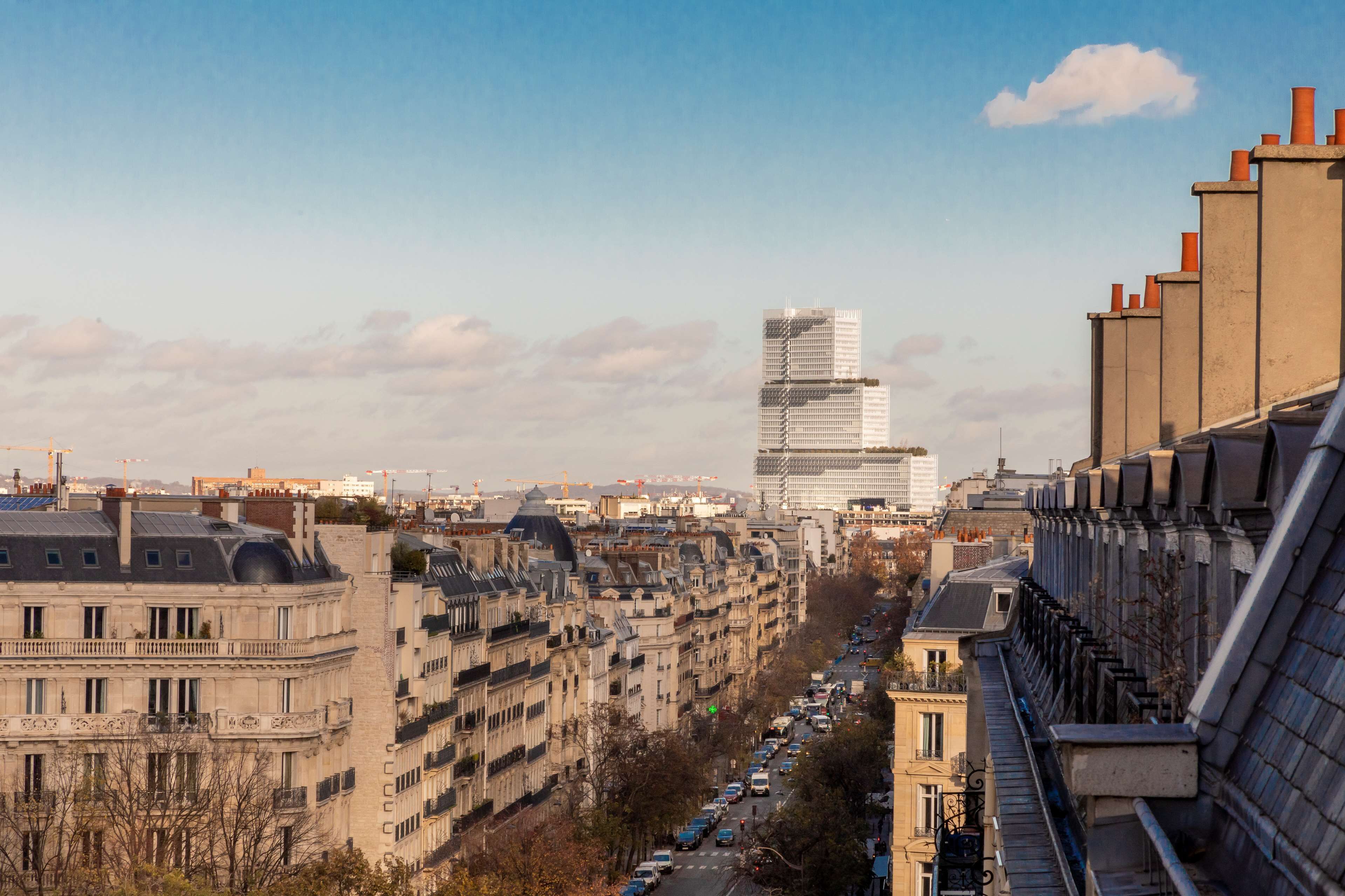 Un paisaje urbano con un moderno rascacielos destacado, edificios históricos y una calle concurrida.