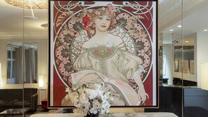 A framed artwork of a woman in a detailed dress, a vase of white flowers, and a marble table in a modern room with a large mirror and a hanging light fixture. - Hotel Elysées Céramic (Paris)