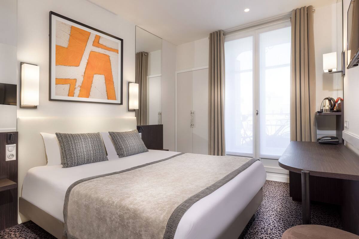 Une chambre d’hôtel avec un grand lit, un bureau, une chaise, un miroir et une fenêtre avec des rideaux.