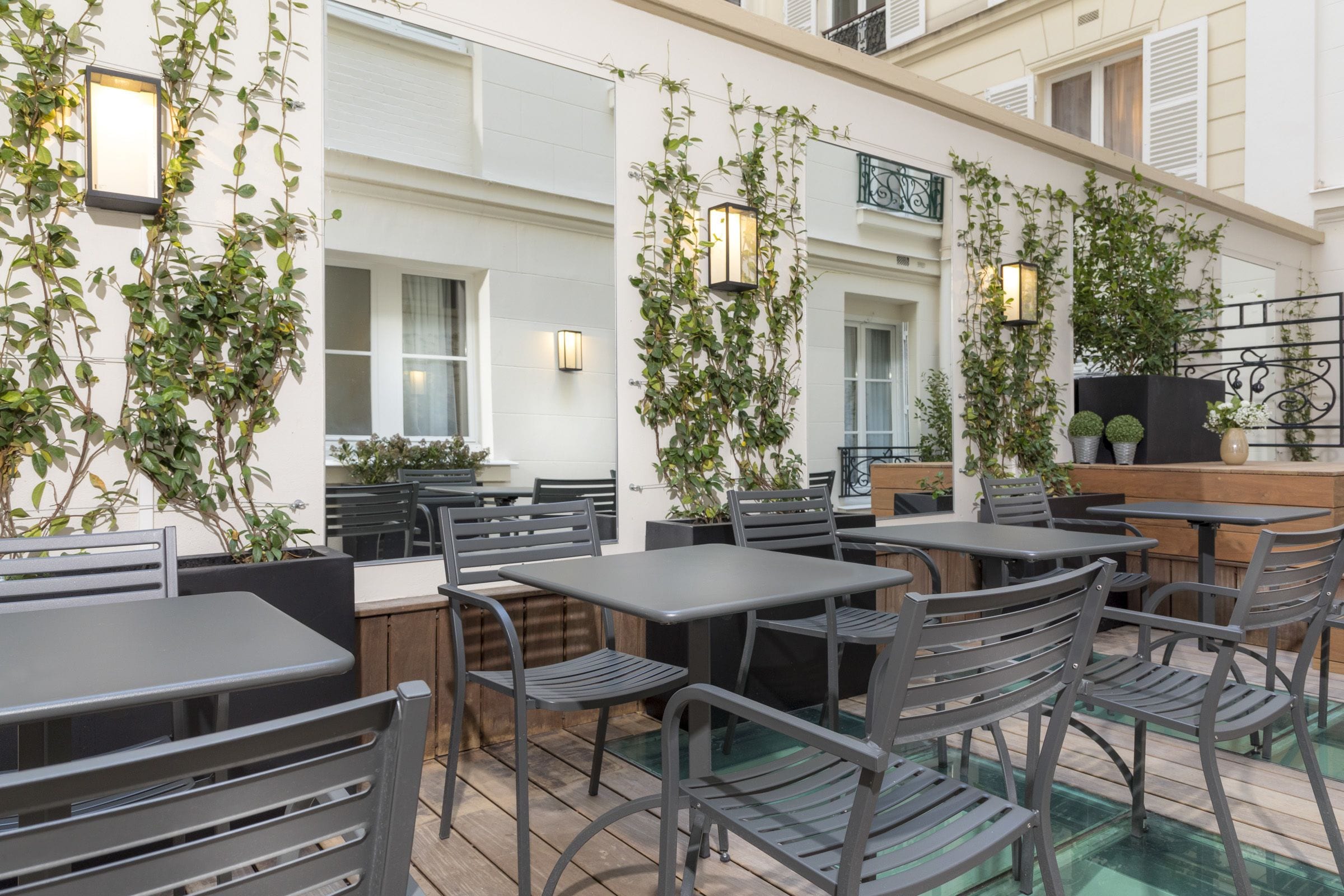 An outdoor patio with tables and chairs, surrounded by greenery and architectural details.