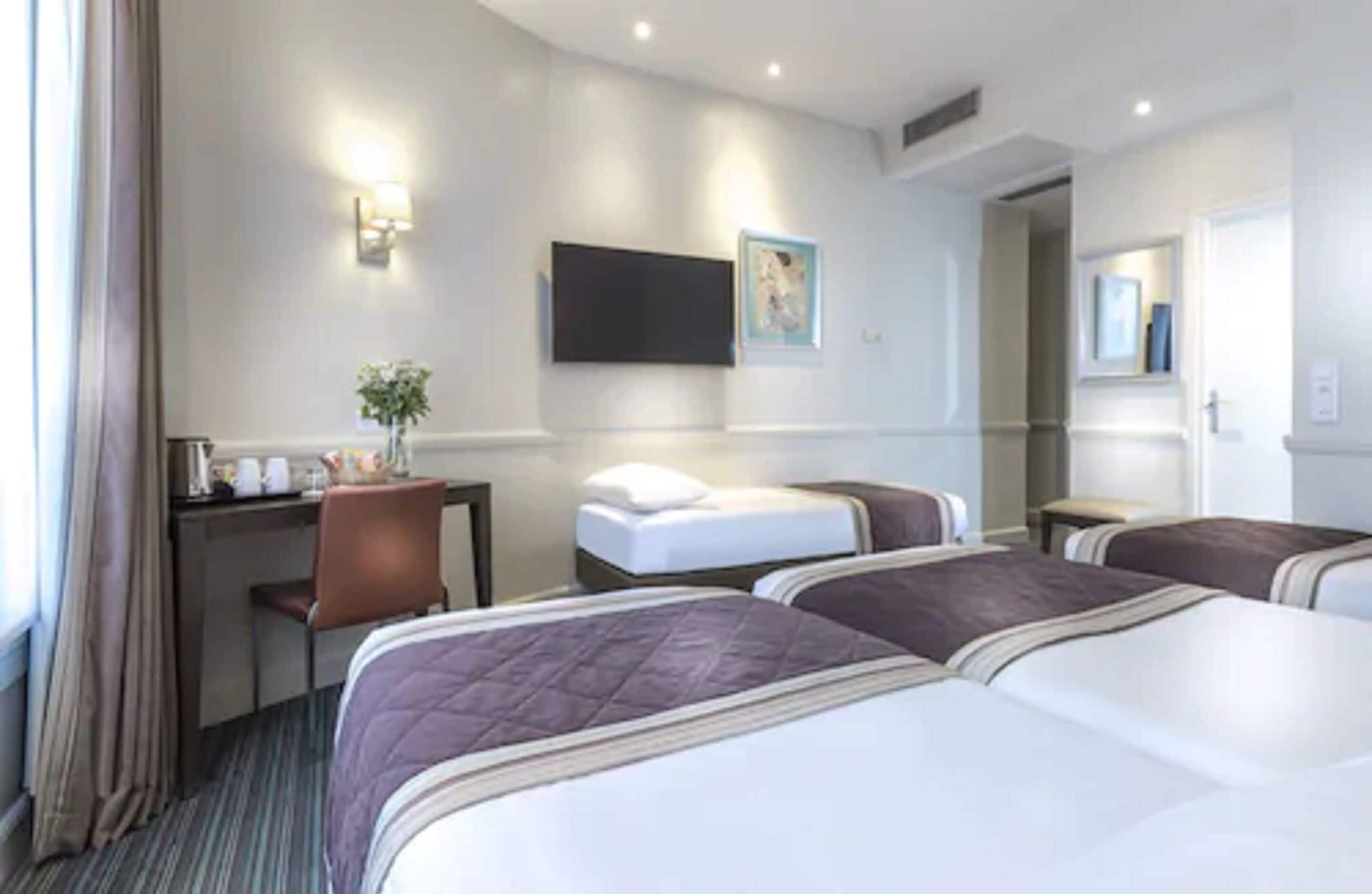 A hotel room with two beds, a desk, a chair, a flat-screen TV, and a painting on the wall.