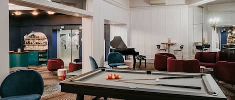 A billiards table in a well-lit room with modern furniture and a piano.