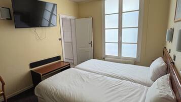 A hotel room with two beds, a TV, a window with blinds, a door, and a small table.