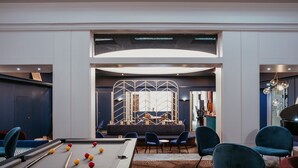 A pool table with balls, a seating area with chairs, and a bar with a piano.