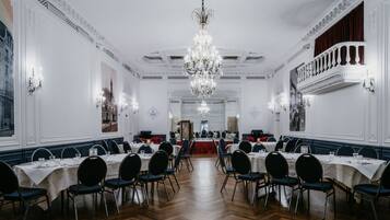 Uma sala de jantar formal com várias mesas, cadeiras e um lustre.