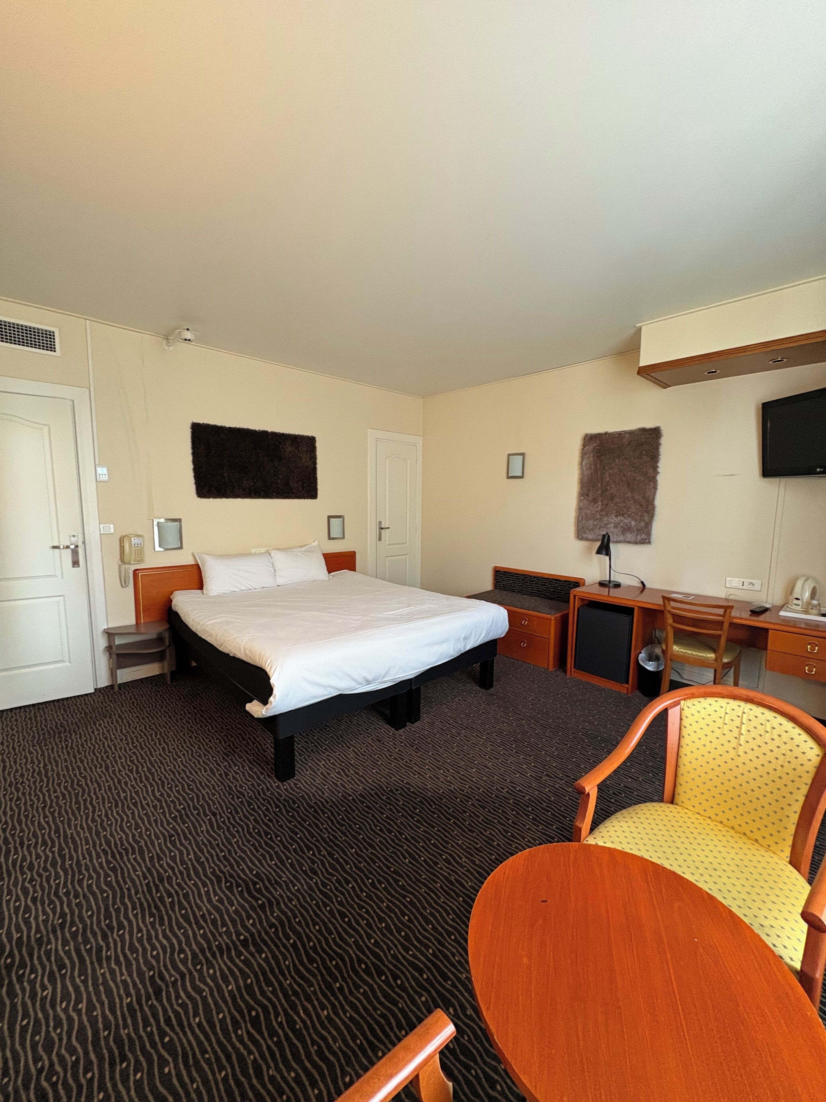 A hotel room with a bed, a desk, a chair, a television, and a small cabinet.