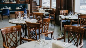 A restaurant interior with round tables, wooden chairs, and a stained glass window.