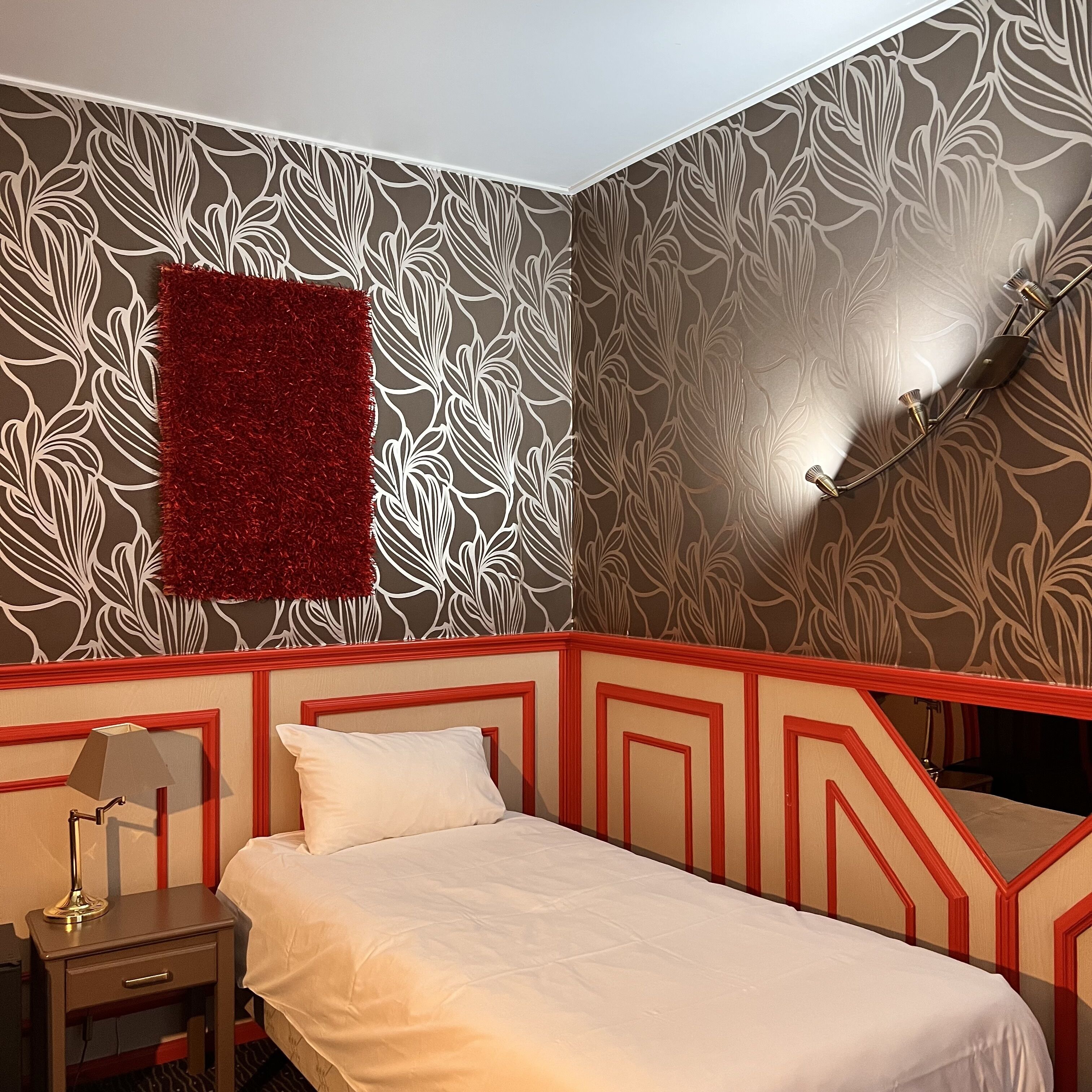Une chambre à coucher avec un lit, une table de chevet, un tapis rouge et un luminaire fixé au mur.