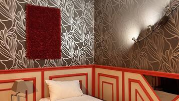 Un dormitorio con cama, una mesita de noche, un tapete rojo y una lámpara fijada a la pared.