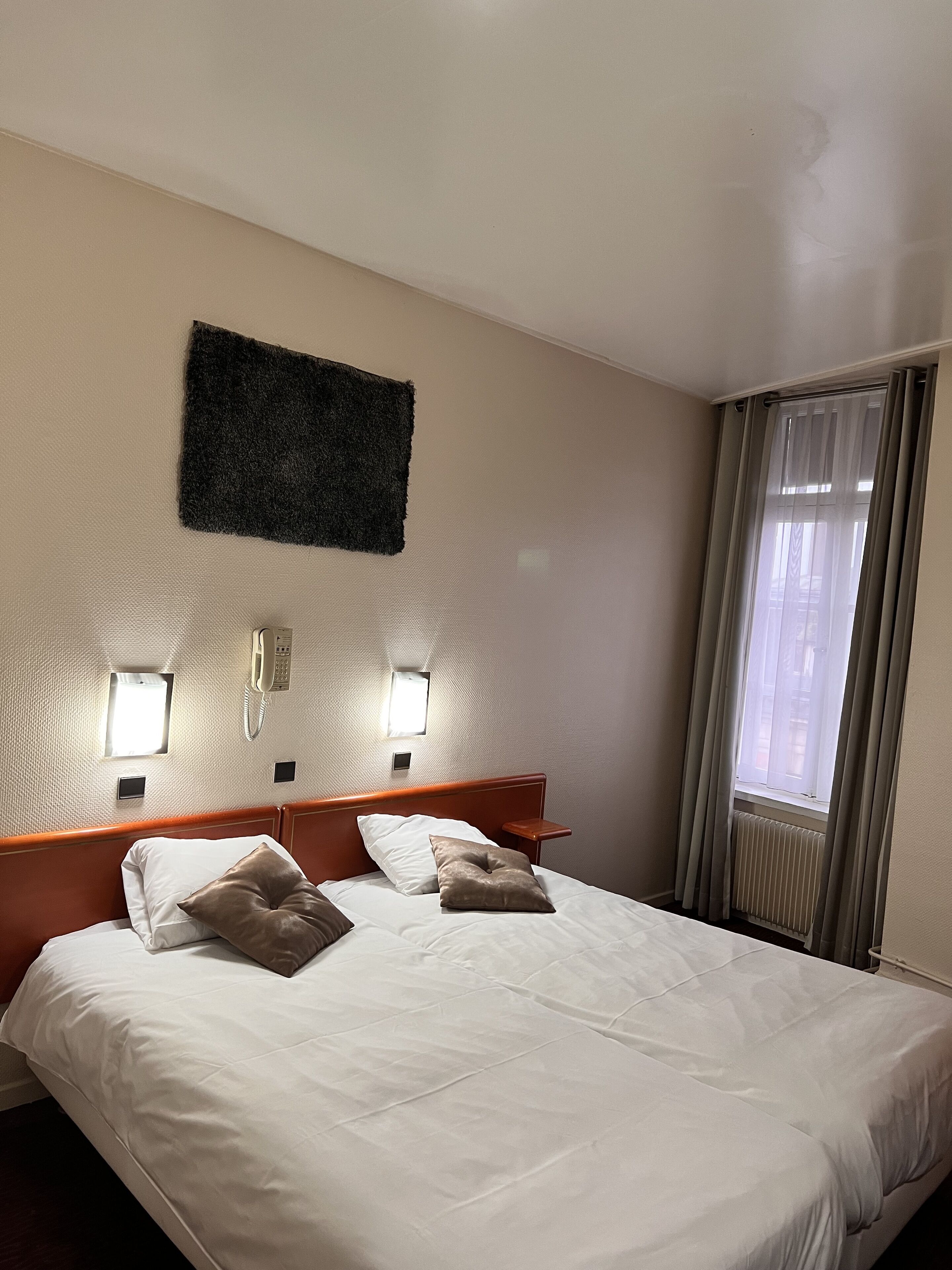 Ein Hotelzimmer mit einem großen Bett, zwei Nachttischen, einem an der Wand montierten Telefon und einem Fenster mit Vorhängen.