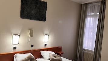 Ein Hotelzimmer mit einem großen Bett, zwei Nachttischen, einem an der Wand montierten Telefon und einem Fenster mit Vorhängen.