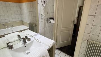 A bathroom with a double sink, a mirror, a towel rack, a hairdryer, and a door leading to another room.