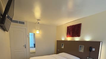 A hotel room with a bed, a desk, a telephone, and a wall-mounted TV.
