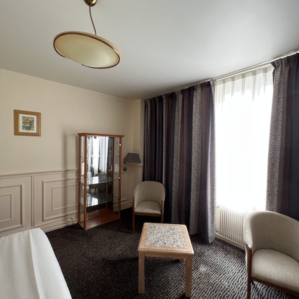 A hotel room with a bed, a small table, a chair, a mirror, and a window with curtains.