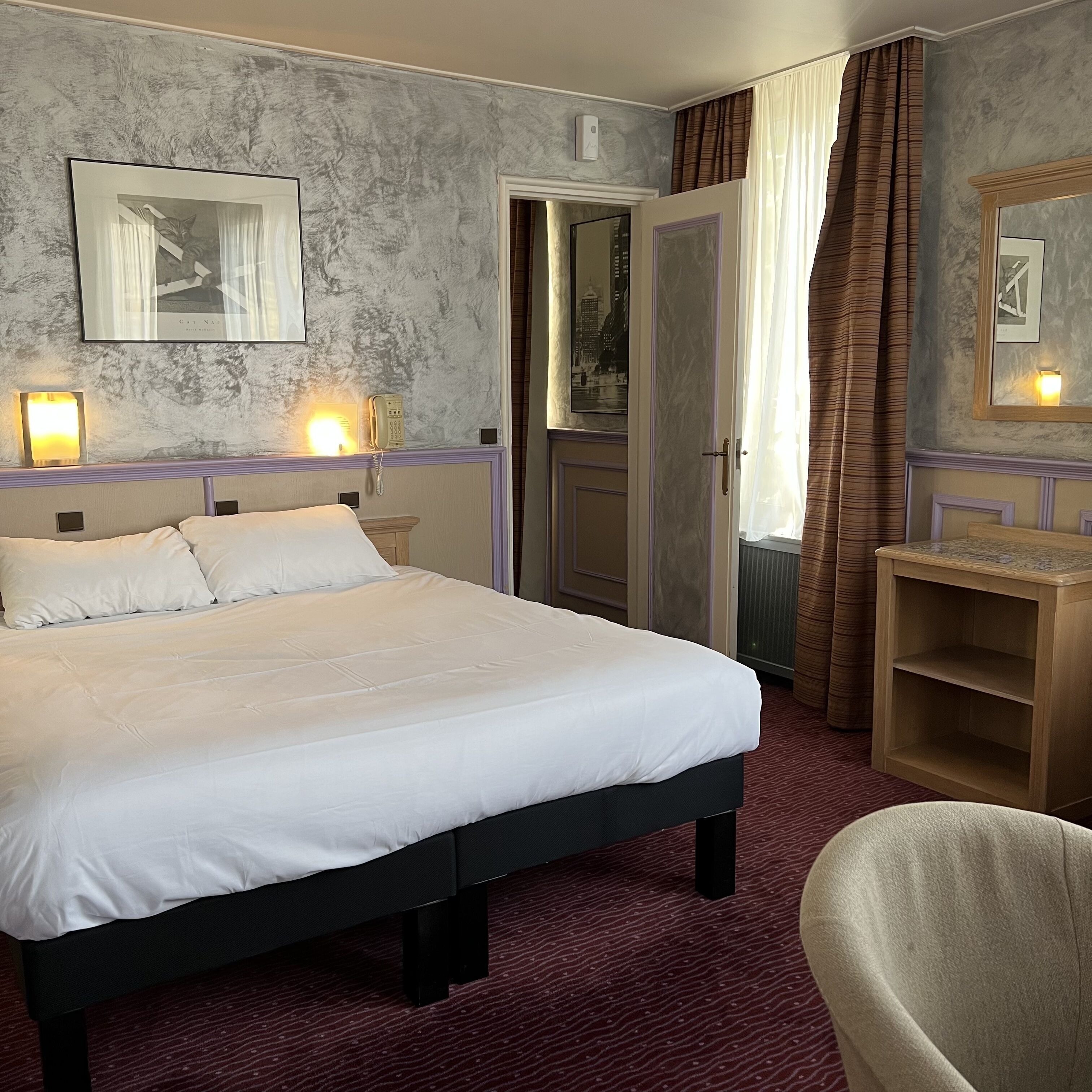 Quarto de hotel com uma cama grande, abajures, uma escrivaninha e uma cadeira.