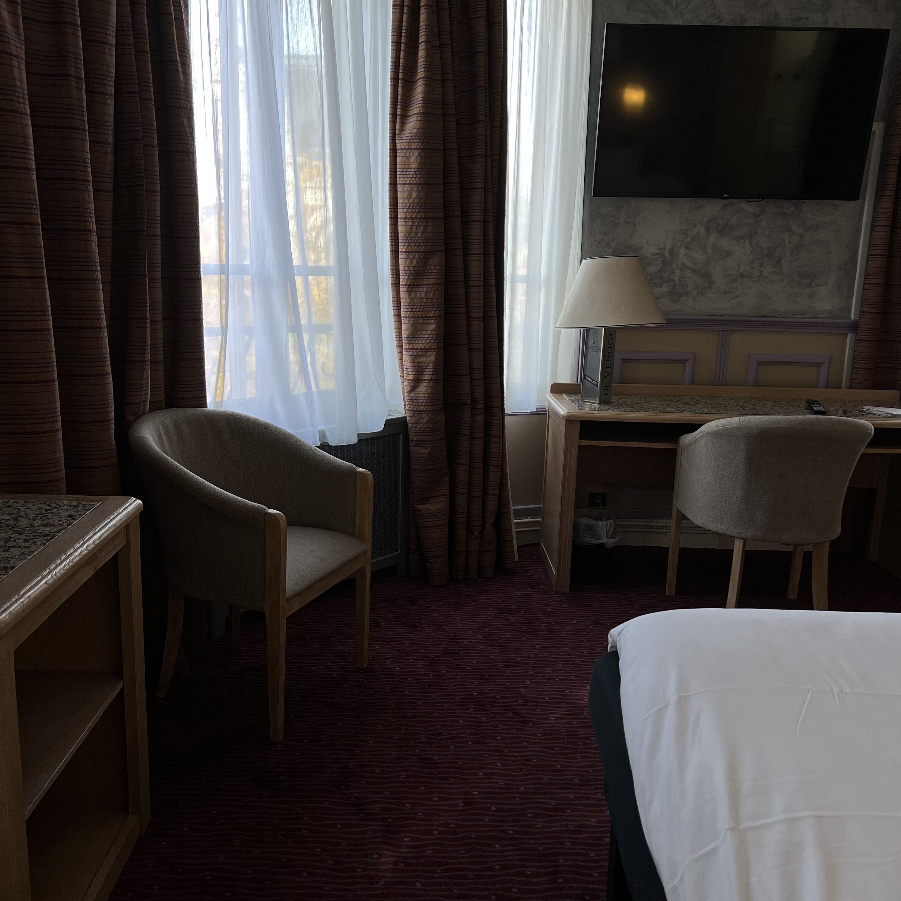 A hotel room with a bed, a desk, a chair, a TV, and a window with curtains.