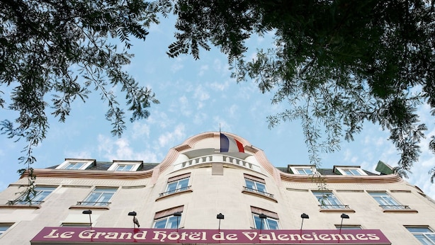 The facade of Le Grand Hotel de Valencia with a prominent sign, multiple windows, and a flag.